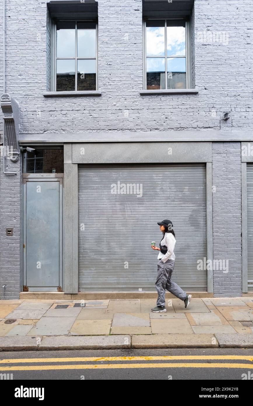 GV-Ansicht einer Solo-Frau, die an einem geschlossenen Geschäft in Shoreditch East London, Großbritannien, vorbeiläuft Stockfoto