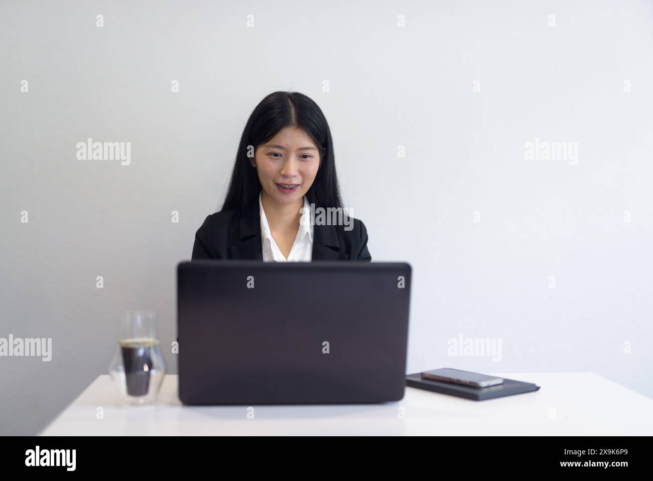 Asiatische Geschäftsfrau mit Laptop im Büro, Kaffee und Notebooks auf dem Schreibtisch. Professionelle Einstellung vor weißem Hintergrund mit Copyspace. Stockfoto