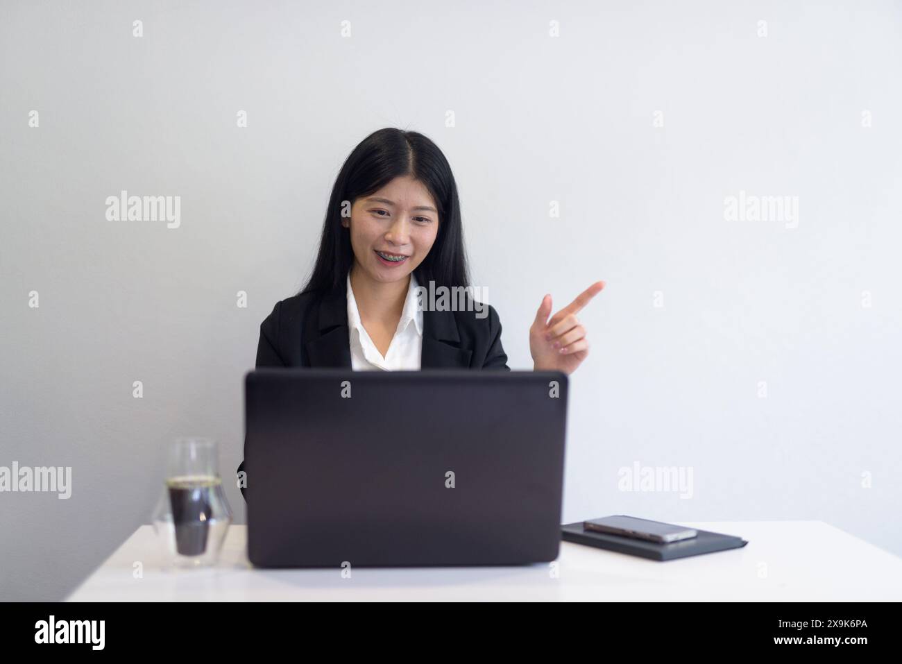 Asiatische Geschäftsfrau mit Laptop im Büro, Kaffee und Notebooks auf dem Schreibtisch. Professionelle Einstellung vor weißem Hintergrund mit Copyspace. Stockfoto