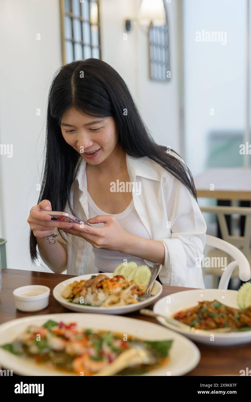 In einem Restaurant macht eine junge Frau glücklich ein Foto mit ihrem Handy und nimmt ihren modernen Lebensstil auf Stockfoto