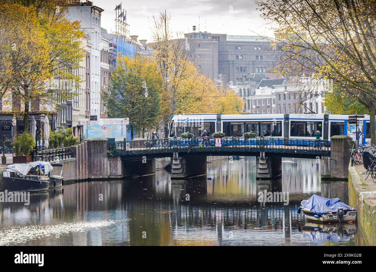 Amsterdam, Niederlande, 20. November 2022. Friedlicher Vormittag von Amsterdam im Herbst mit Straßenbahn, Brücke, Gebäuden, Fahrrädern, Bäumen, und Reflexionen in der CA Stockfoto