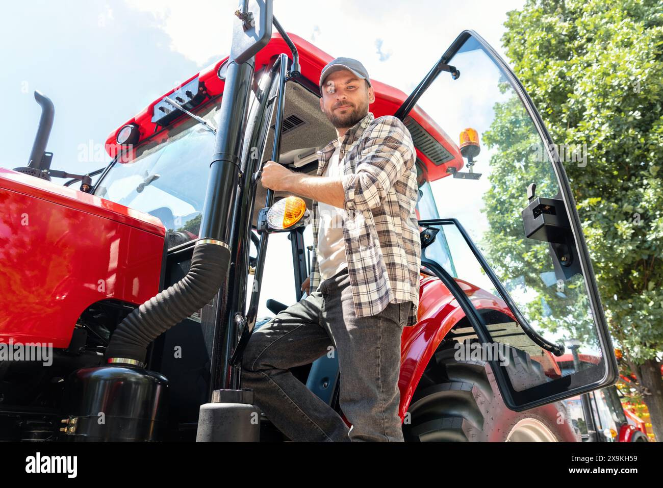 Fotografie eines Landwirtschaftsmannes, der neben seinem Traktor posiert. Stockfoto