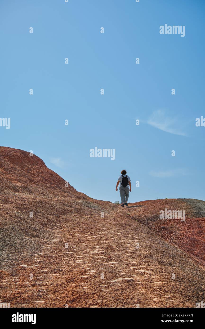 Vertikales Poster eines Touristen, der einen Berg hinaufklettert, während er in den roten Bergen wandert, ein Poster für eine Einladung zum Reisen mit Kopierraum für Stockfoto