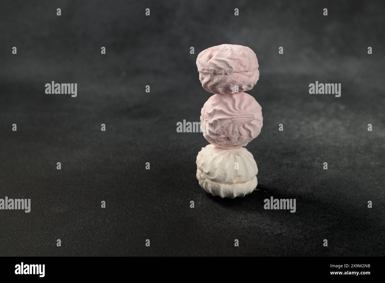 Weiche und flauschige weiße und rosafarbene Marshmallows bilden einen schönen Kontrast zu einem auffälligen schwarzen Hintergrund. Eine optisch ansprechende Komposition, die perfekt für Concept ist Stockfoto