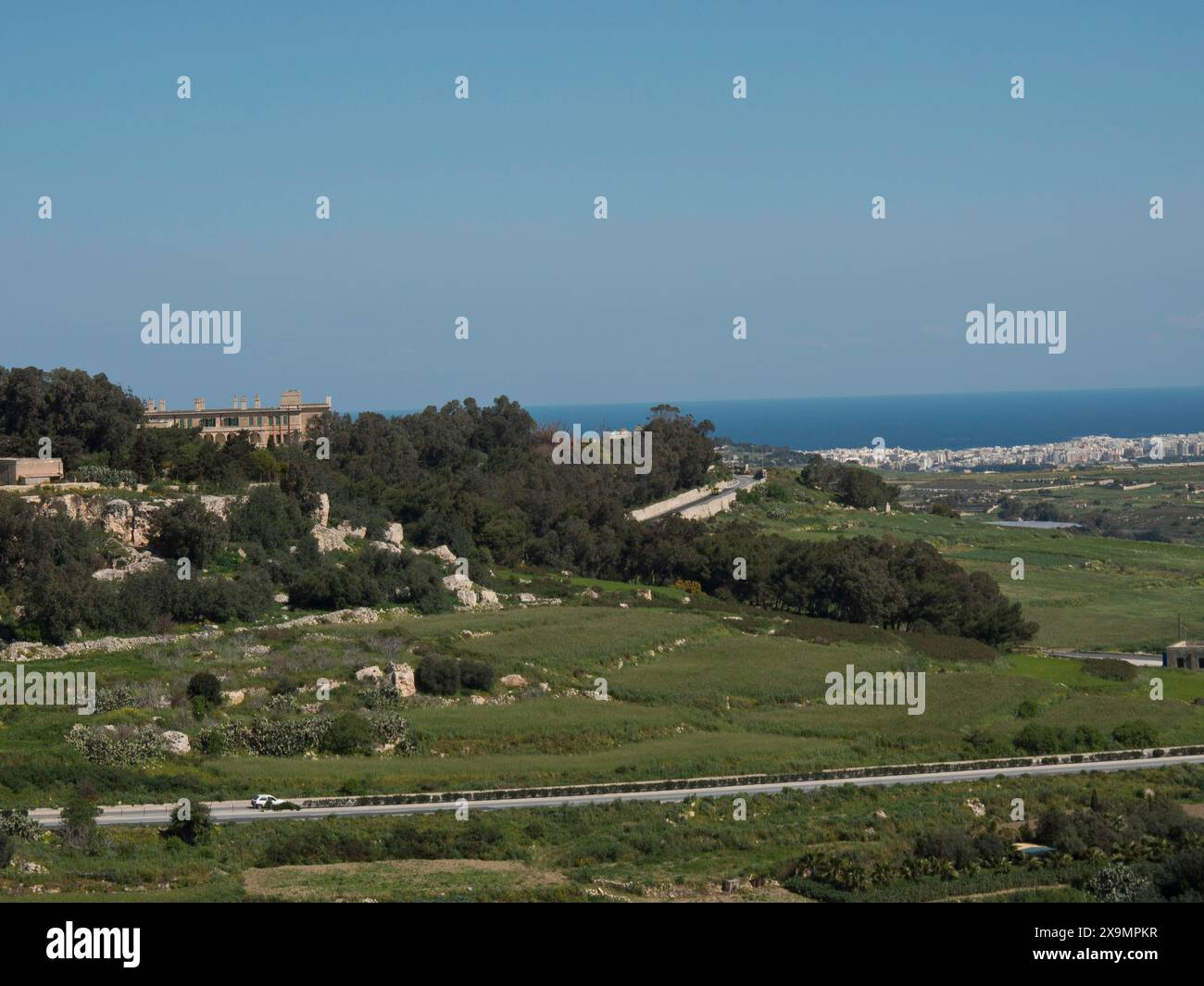 Riesige grüne Landschaft mit Hügeln, Bäumen und einer Stadt am Horizont unter klarem Himmel, die Stadt mdina auf der Insel malta mit historischen Häusern Stockfoto