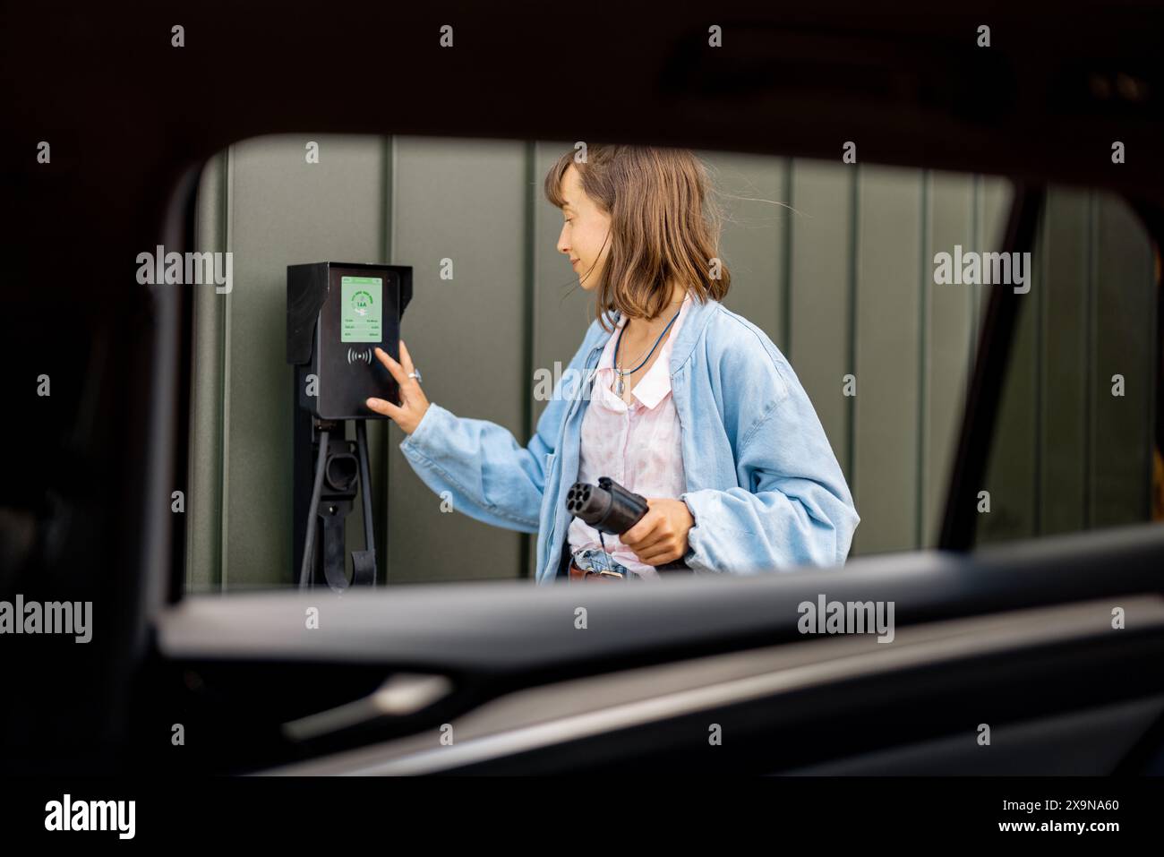 Frau, die Elektroauto mit Ladestation zu Hause auflädt Stockfoto