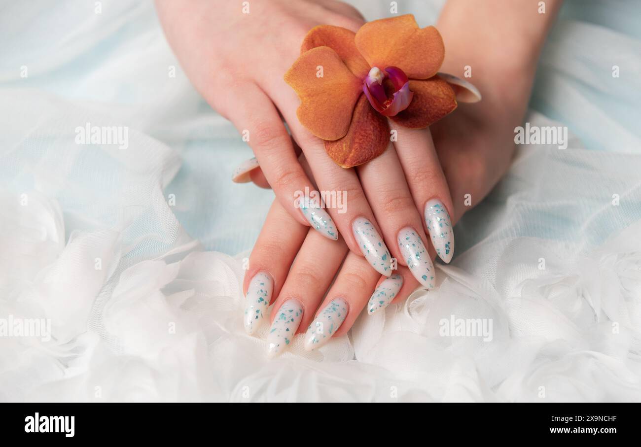 Eine Nahaufnahme zeigt eine Person Hand mit komplizierten, floralen Nailarten, die zart eine Orangenblüte umhüllt. Die umliegende weiche, schwungvolle Textur Stockfoto