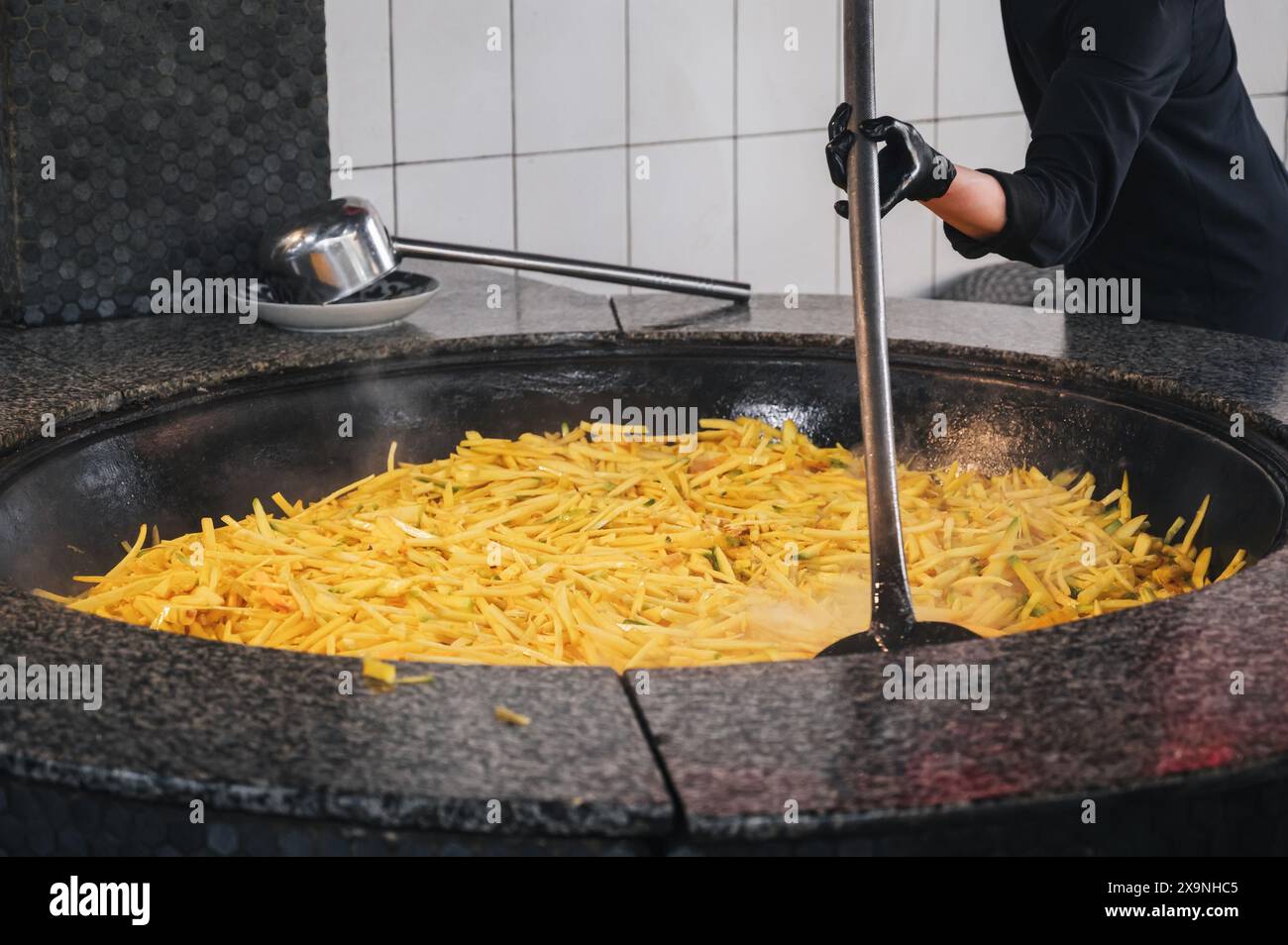 Männliche Köche dünsten gelbe Karotten in einem Kessel, um traditionelle usbekische Pilaw in der Küche eines Restaurants in Usbekistan zu kochen Stockfoto