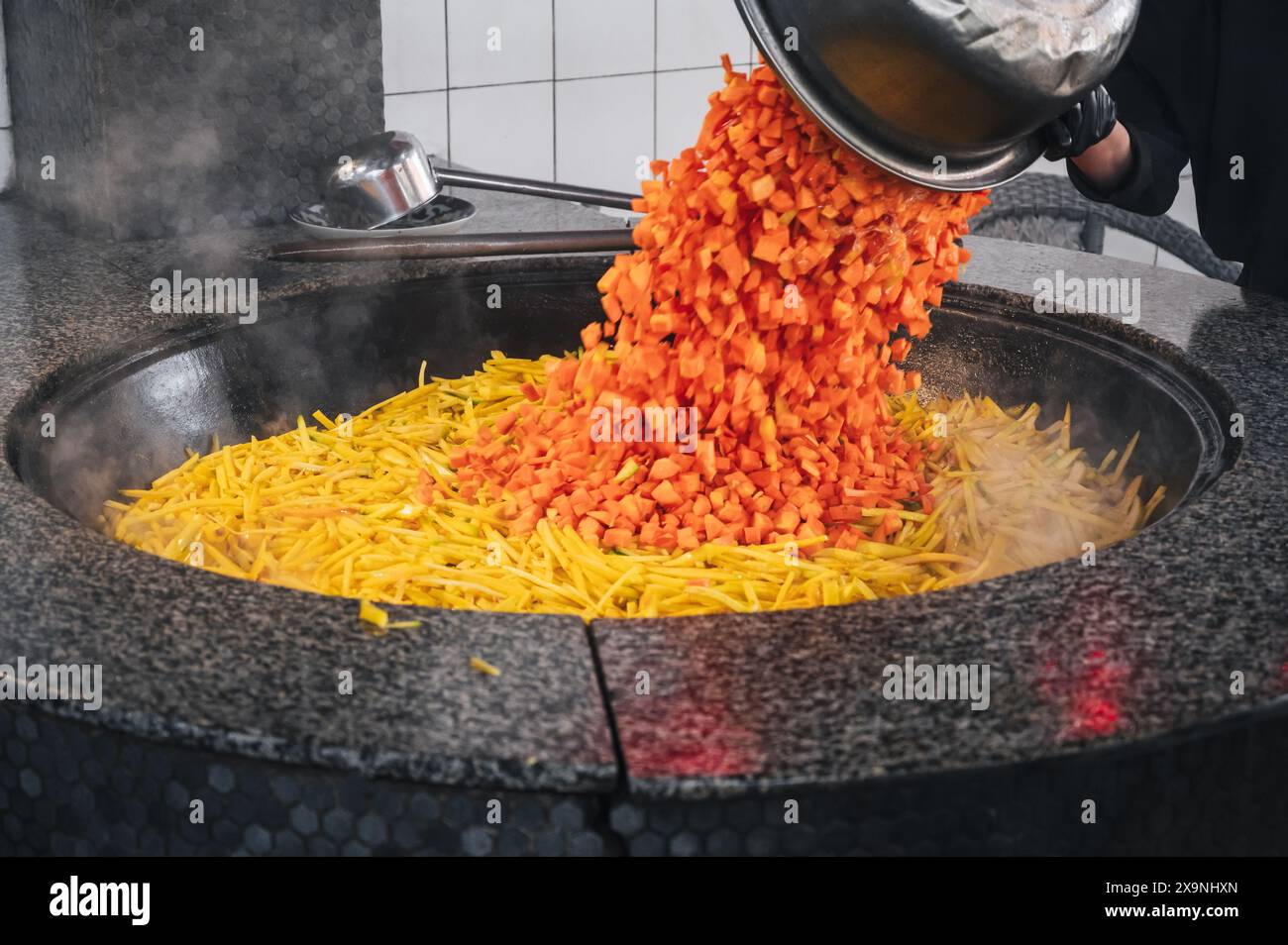 Der Küchenchef fügt Karotten in einen Kessel, um in der Küche eines Restaurants in Usbekistan traditionelle usbekische Pilaw zu kochen Stockfoto