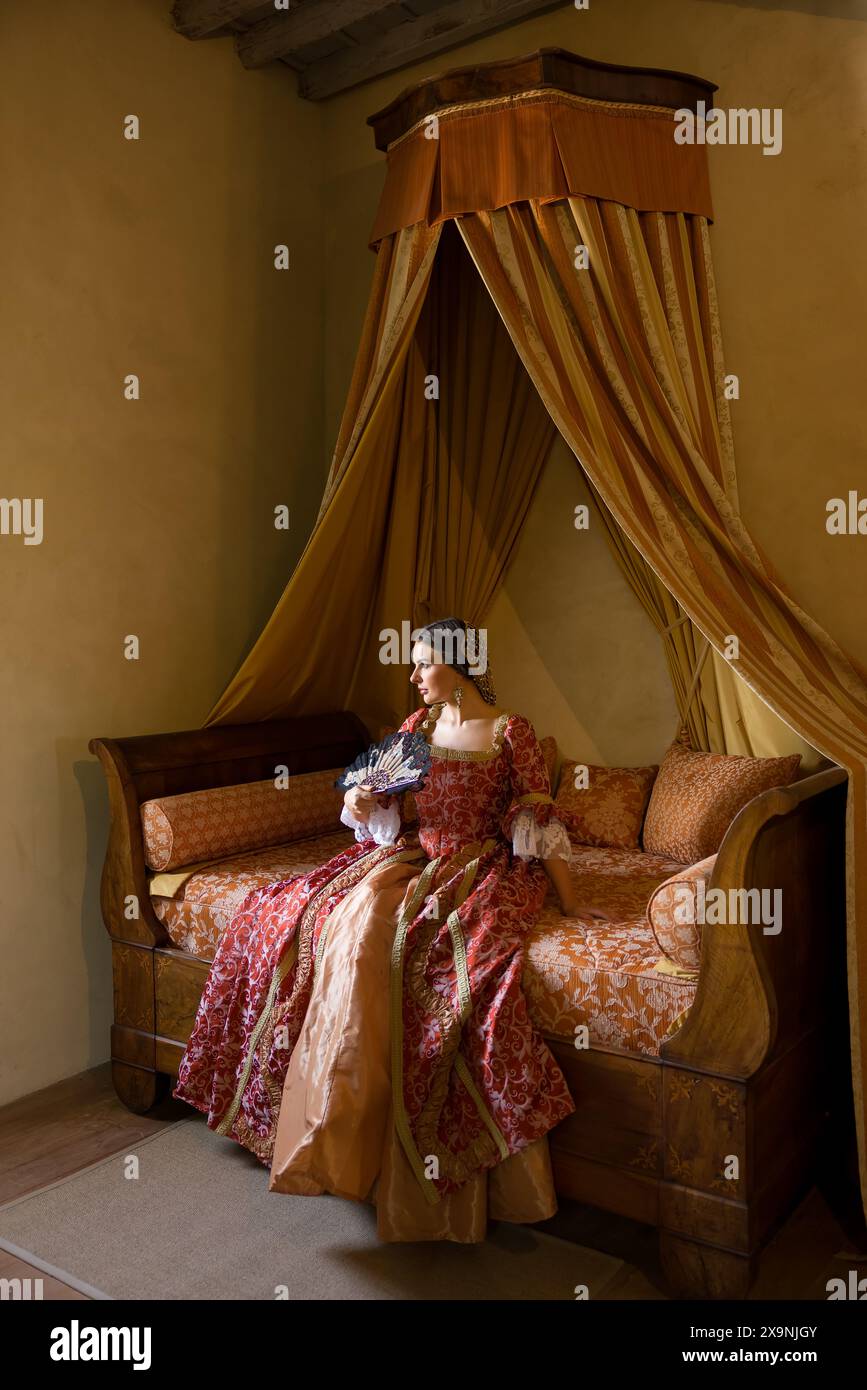 Renaissance-Dame in spätmittelalterlichem Kleid sitzt auf einem schönen Himmelbett in ihrem Schloss Schlafzimmer Stockfoto