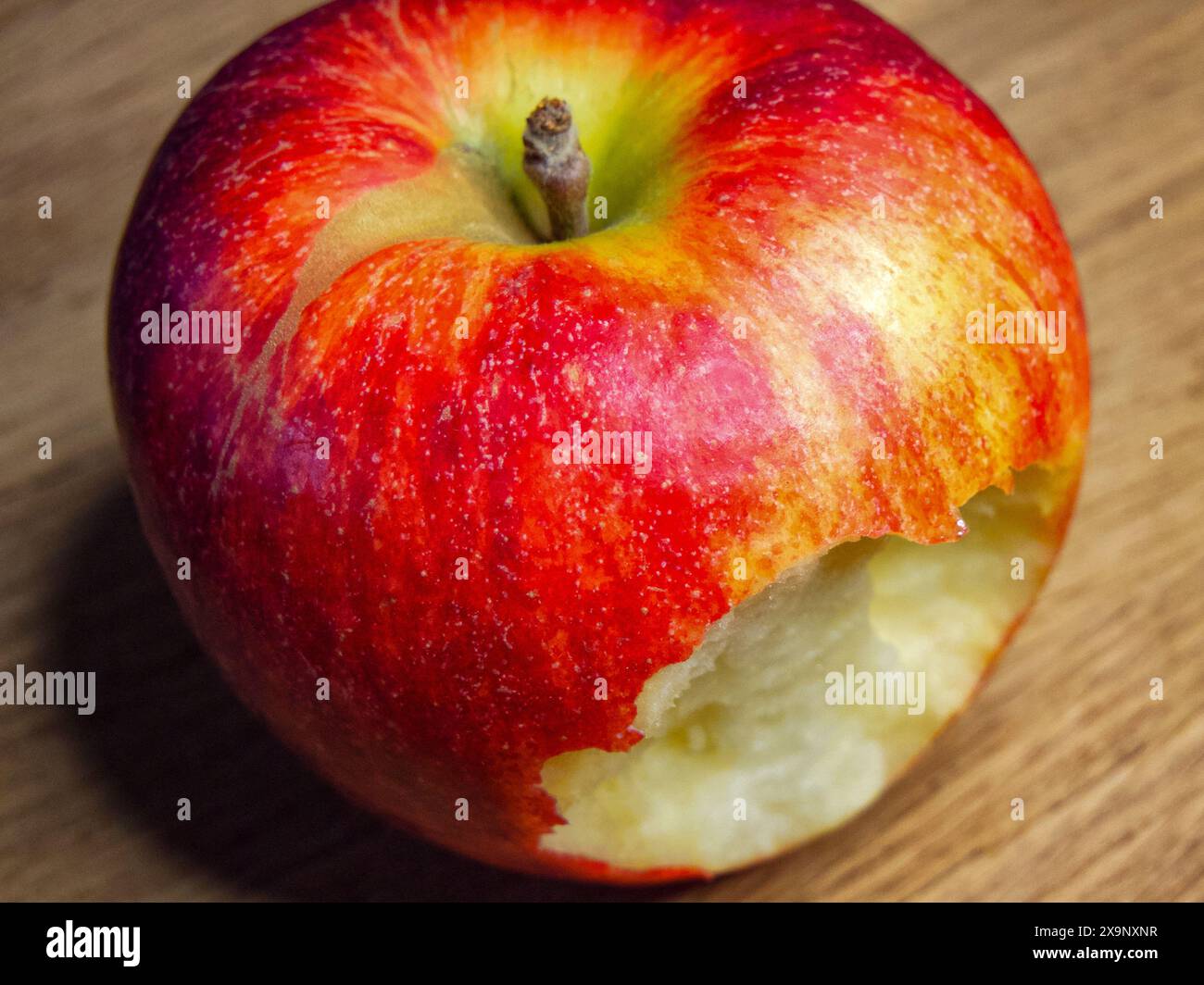 Frisch Gebissener Apfel. Ein roter Apfel mit einem Biss, der auf einer Holzoberfläche liegt und Themen der Gesundheit und Frische hervorruft. Stockfoto