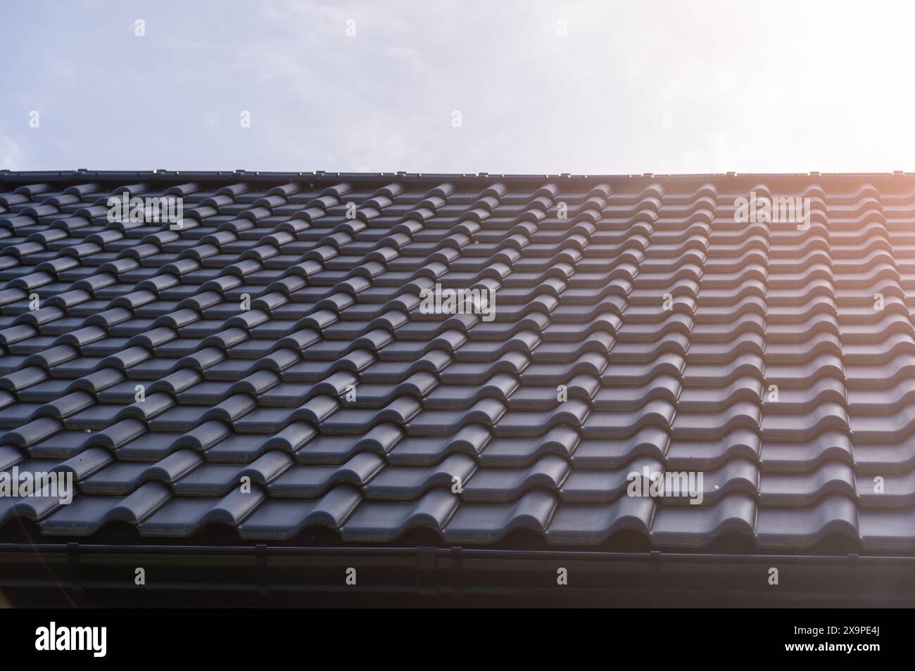 Der Close-up-Winkel eines modernen, schwarz gekachelten Dachs erfasst die detaillierte Struktur und die Kurven unter einem hellen Sonnenlicht und unterstreicht die moderne Architektur Stockfoto