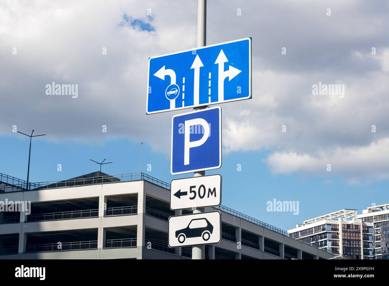 Ein blaues Parkschild mit Pfeilen nach rechts ist sichtbar. Das Schild befindet sich in der Stadt, in der Nähe eines Gebäudes und einer Tankstelle. Der Himmel ist klar Stockfoto