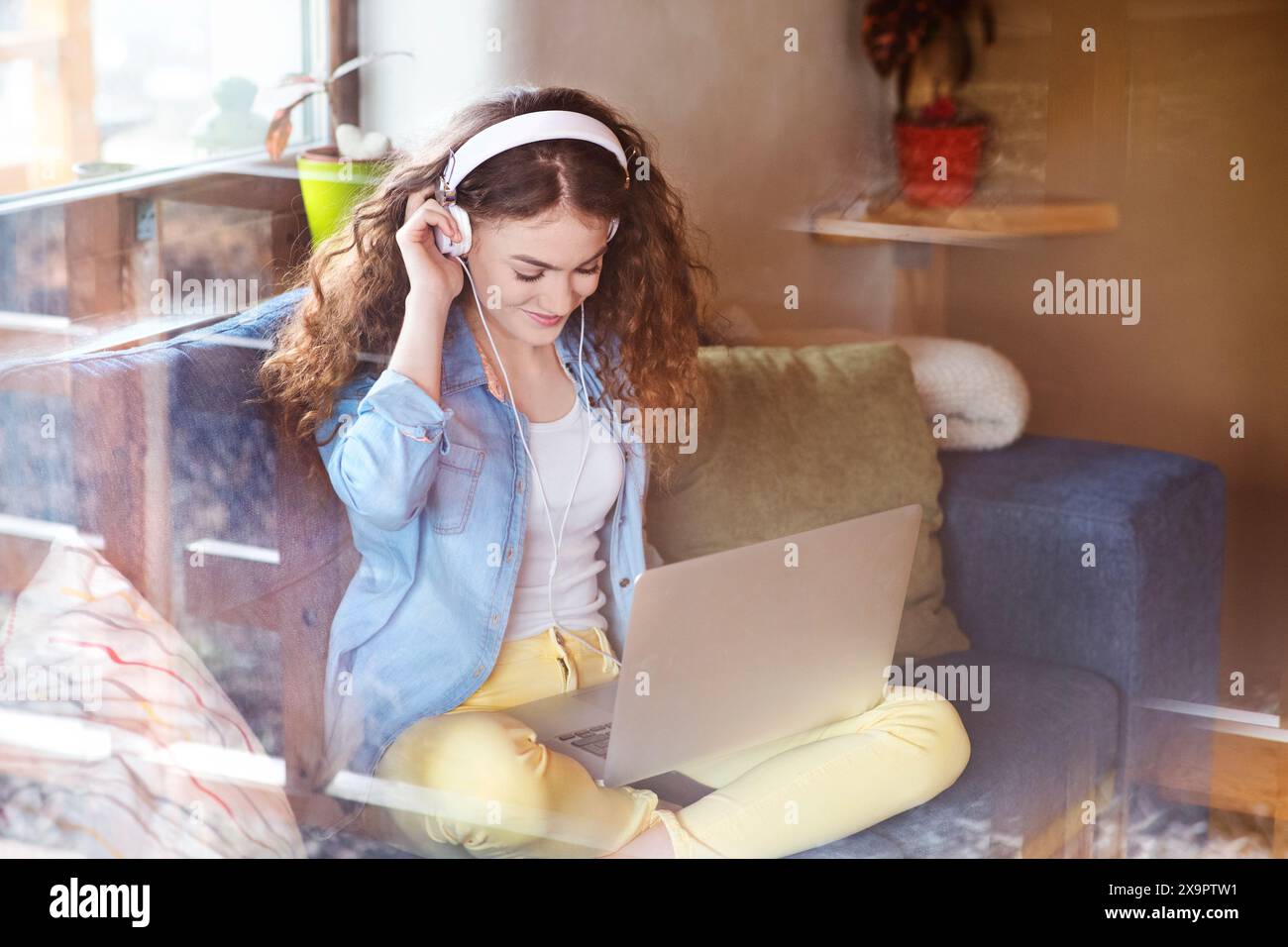Schöne Frau mit lockigem Haar, die Kopfhörer trägt, Musik hört, positive Affirmationen. Stockfoto