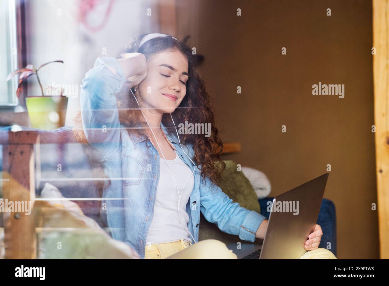 Schöne Frau mit lockigem Haar, die Kopfhörer trägt, Musik hört, positive Affirmationen. Stockfoto