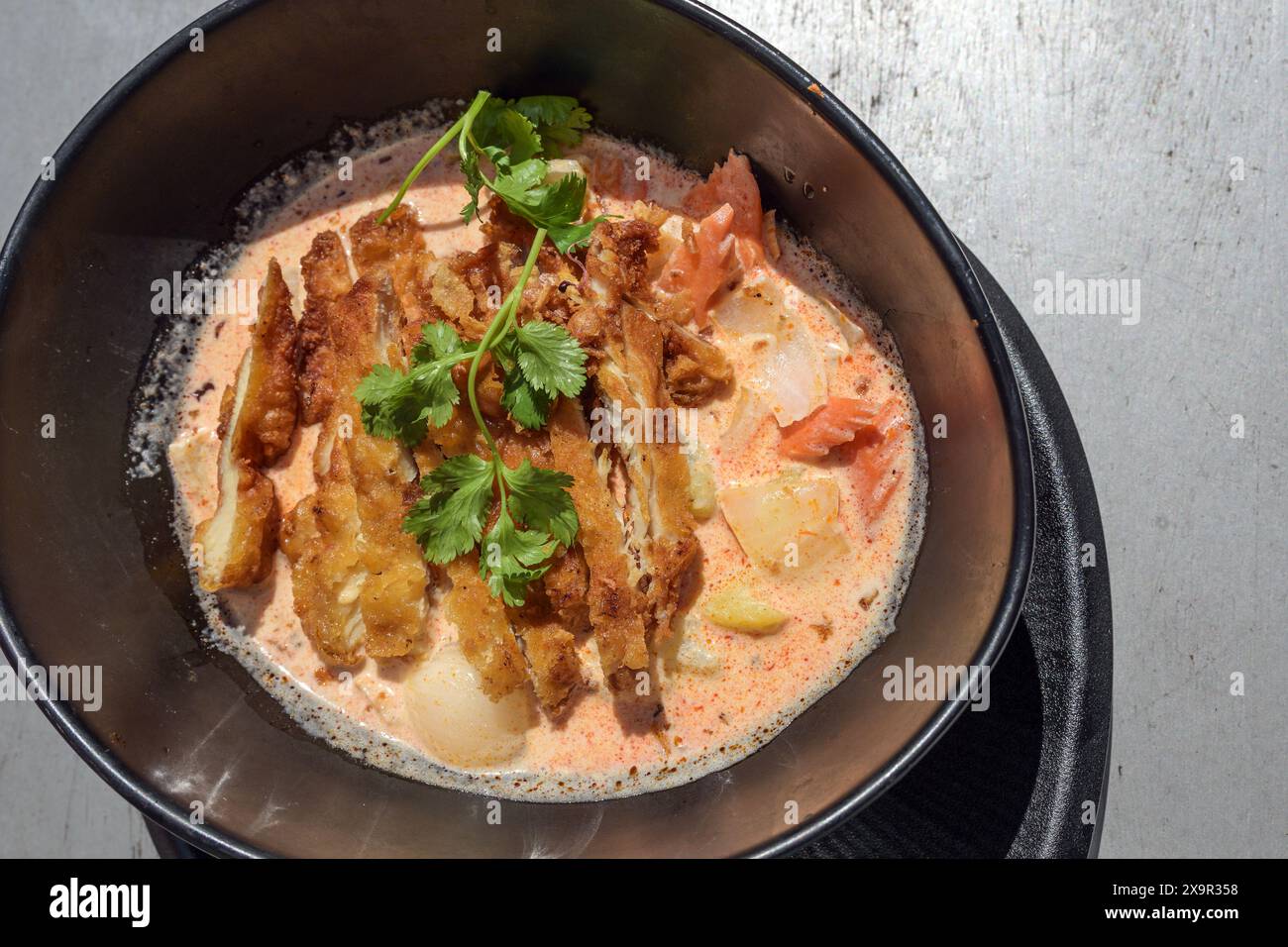 Knusprige gebratene Hähnchenscheiben auf einem scharfen Gemüsecurry mit Koriandergarnitur in einer schwarzen Schüssel, asiatische Mahlzeit, Blick von oben Stockfoto