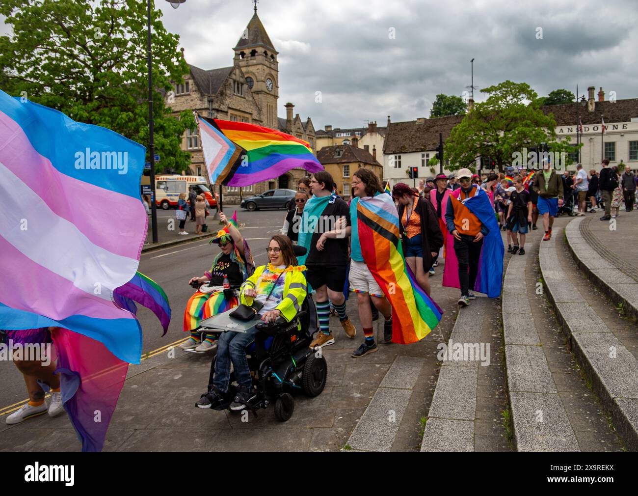 Menschen, die an einem bewölkten Tag am 1. Juni 2024 in Calne Wiltshire mit Regenbogenflaggen und farbenfrohen Outfits teilnehmen Stockfoto
