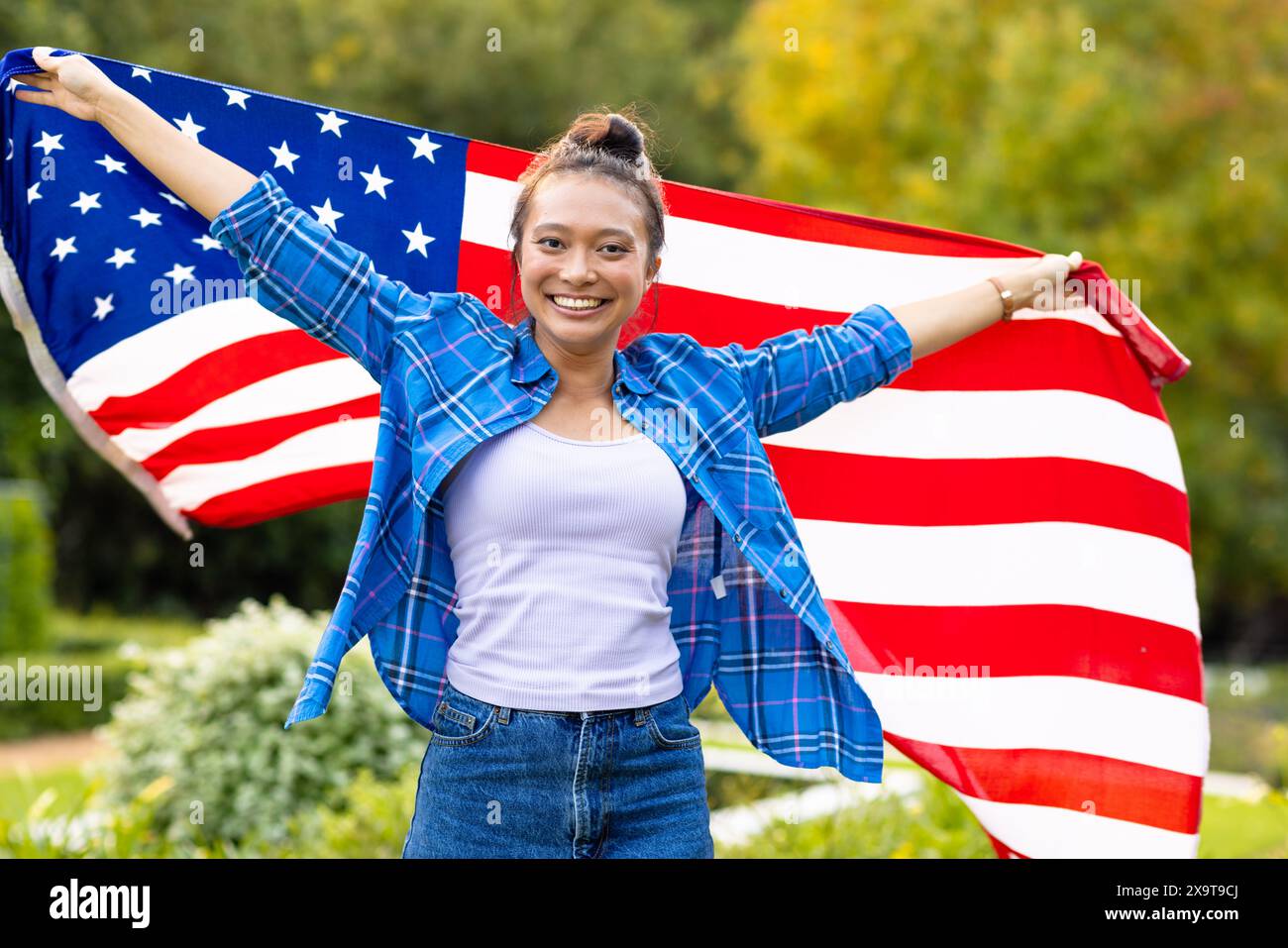Porträt einer glücklichen asiatischen Frau mit breiten Armen und mit Flagge der usa im Garten Stockfoto