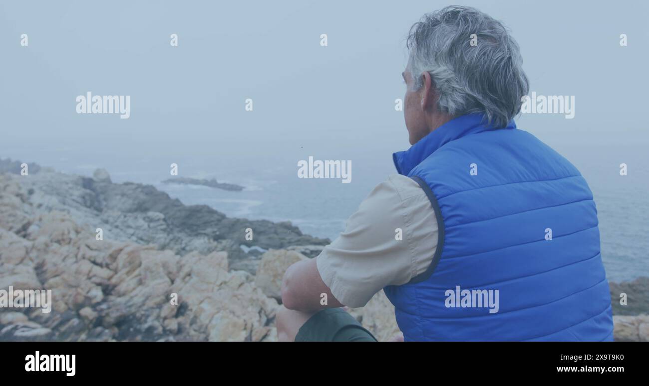 Der kaukasische Mann blickt von einem felsigen Ufer aus auf das Meer, mit Kopierraum Stockfoto