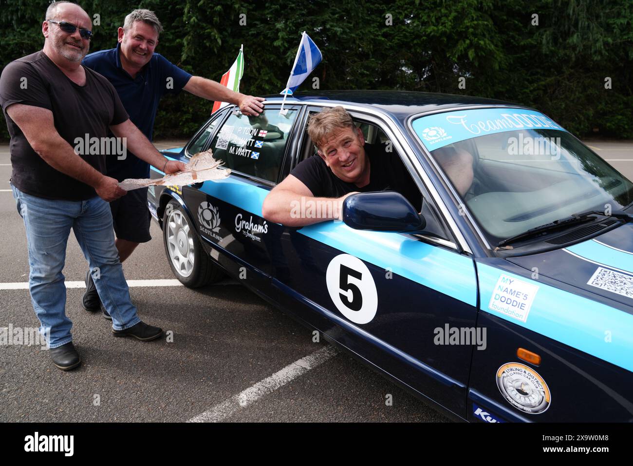 Alan Watt ehemaliger Teamkollege von Doddie Weir mit seinen Freunden Paul Toon (Mitte) und Murray Watt (links) mit ihrem Jaguar Auto, während sie nach der Fahrt durch das Löwengehege im Blair Drummond Safari Park in der Nähe von Stirling Unterstützung holen. vor der Abfahrt zu ihrer Rust to Rome Challenge, um Gelder für die My Name'5 Doddie Foundation zu sammeln. Bilddatum: Freitag, 31. Mai 2024. Stockfoto