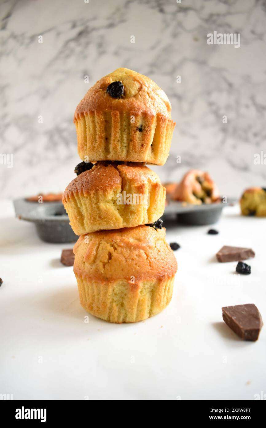 Ein Stapel köstlicher Heidelbeermuffins und Heidelbeeren auf einem weißen Tisch. Gebackene Beeren und Schokolade auf dem Brett. Blaubeermuffins. Stockfoto