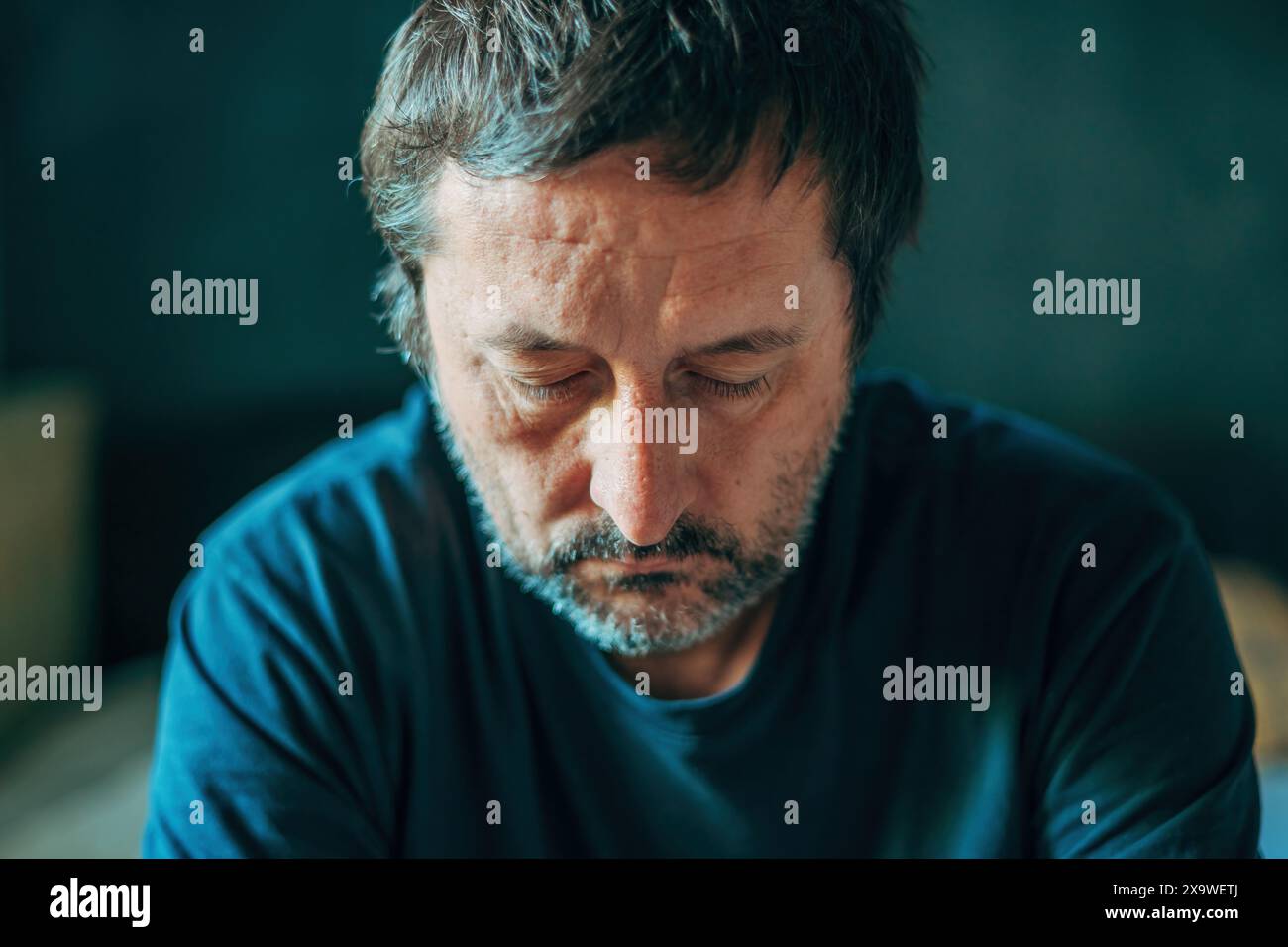 Unglücklicher besinnlicher erwachsener Mann, der in Dunkelkammer denkt, depressiv schmollende männliche Gedanken, selektiver Fokus Stockfoto