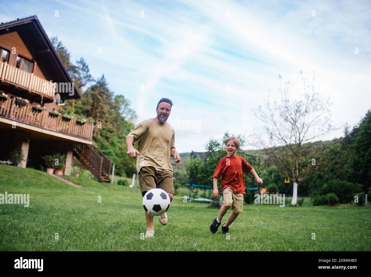 Dad hat Spaß mit dem kleinen Sohn, spielt Fußball, läuft und tritt den Ball. Sie spielen auf einem Rasen vor ihrem Haus. Vaterschaft und Vatertag. Stockfoto