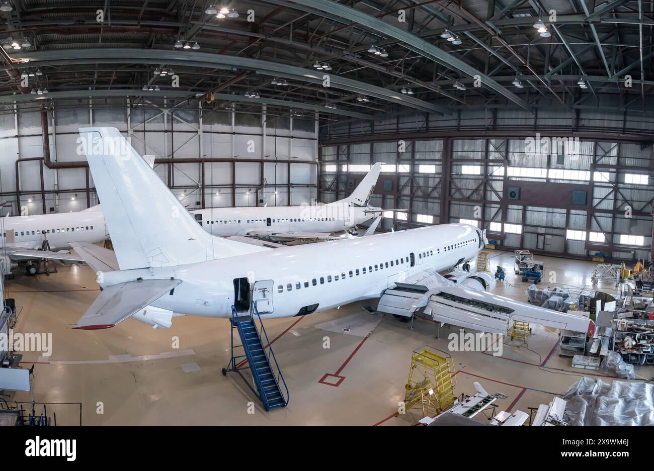 Weiße Passagierflugzeuge im Flugzeughangar. Flugzeuge in Wartung. Überprüfung mechanischer Systeme für den Flugbetrieb Stockfoto