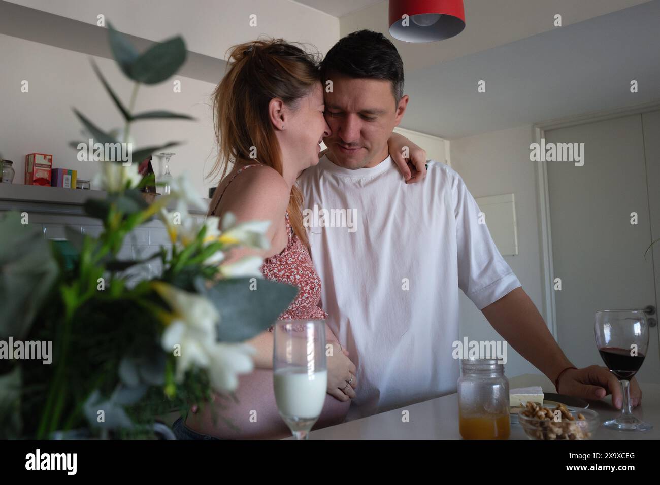 Ein glückliches Paar in der Küche, lachend und umarmen, während sie die Ankunft ihres Babys eifrig erwarten Stockfoto