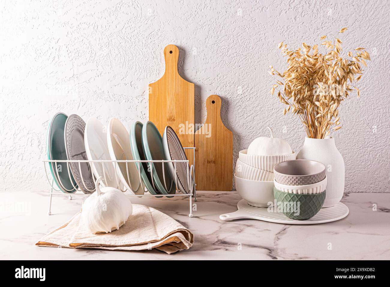 Ein Satz Keramikschalen, Teller in einem Tellertrockner, dekorative Kürbisse auf der Küchenarbeitsplatte. Das Innere einer stilvollen Küche. Vorderansicht Stockfoto