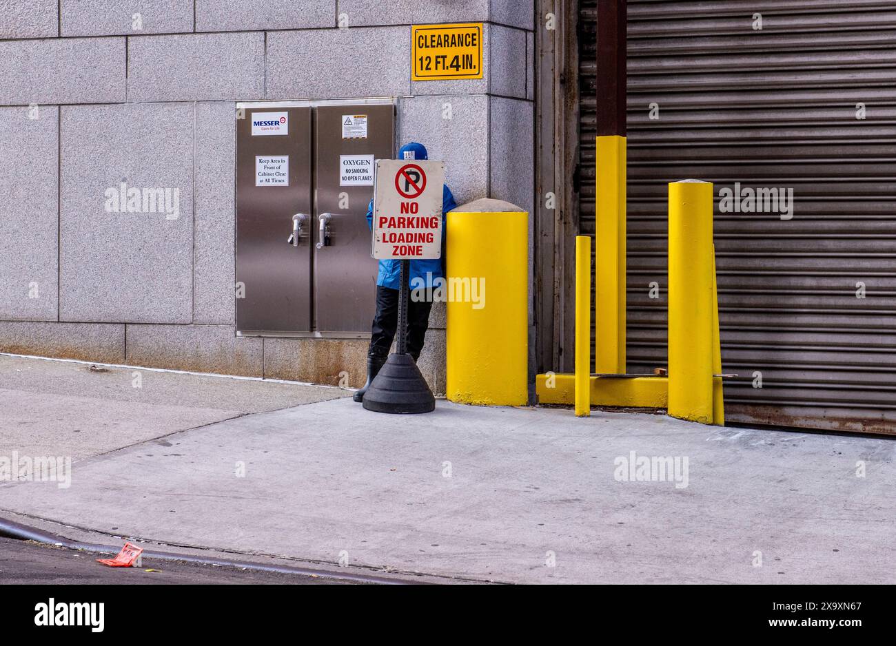 Ein Mann in blau gekleidet versteckt sich hinter einem Parkverbot, umgeben von leuchtend gelben Pollern in New York. Stockfoto