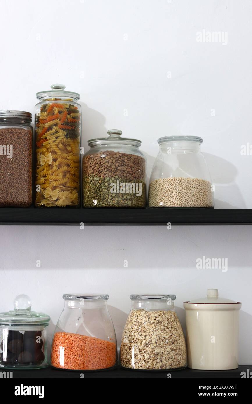 Die Küche ist gut ausgestattet. Regale mit verschiedenen Getreidearten in Gläsern auf weißem Wandhintergrund mit Platz für Text. Verschiedene Samen und Getreide im Glas Stockfoto