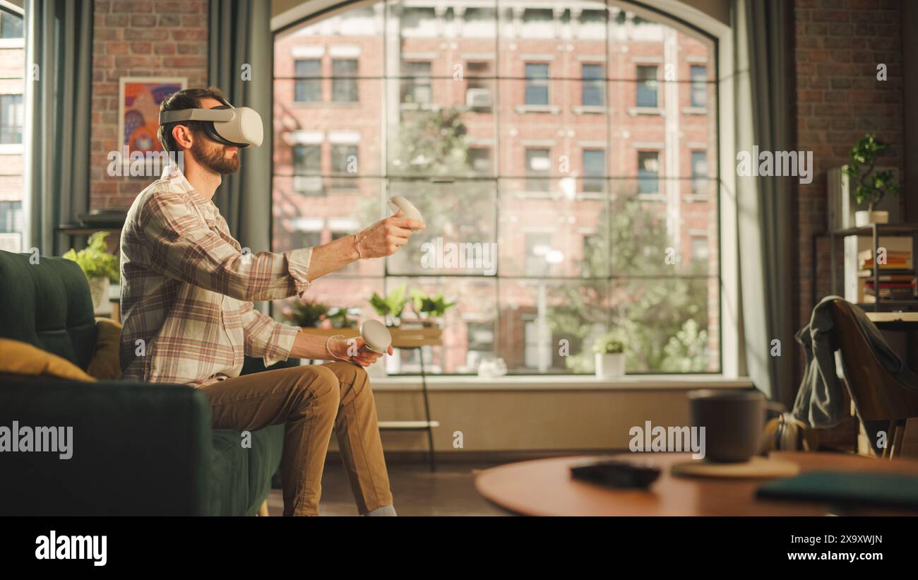 Männlicher Erwachsener, der zu Hause Virtual Reality-Headset und -Controller verwendet. Kreativer Mann, der im Wohnzimmer auf einem Sofa sitzt, VR-Videospiel spielt oder mit speziellen digitalen Tools arbeitet. Stockfoto