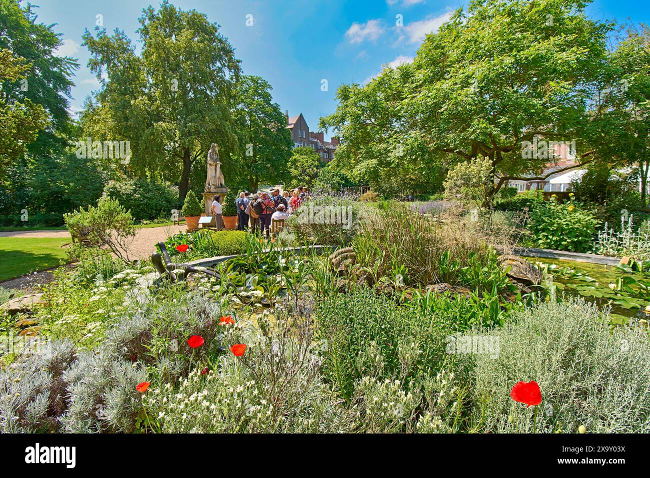 Chelsea Physic Garden der kleine Teich im Frühling und eine Gruppe von Touristen neben der Statue von Hans Sloane Stockfoto
