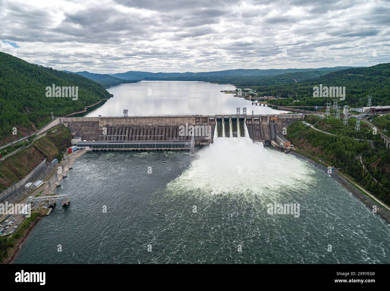 Aus der Vogelperspektive eines Betondamms, der Wasser an bewölkten Tagen in den Fluss abgibt. Wasserentladung im Wasserkraftwerk. Stockfoto