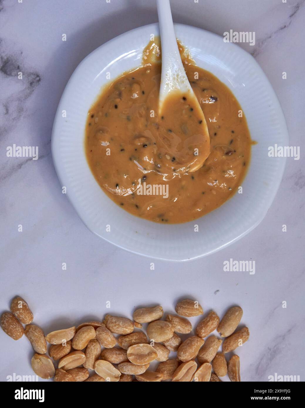 Erdnusspaste mit Samen auf einer weißen Platte mit weißem marmo-Boden und einer Handvoll Erdnüsse an der Seite Stockfoto