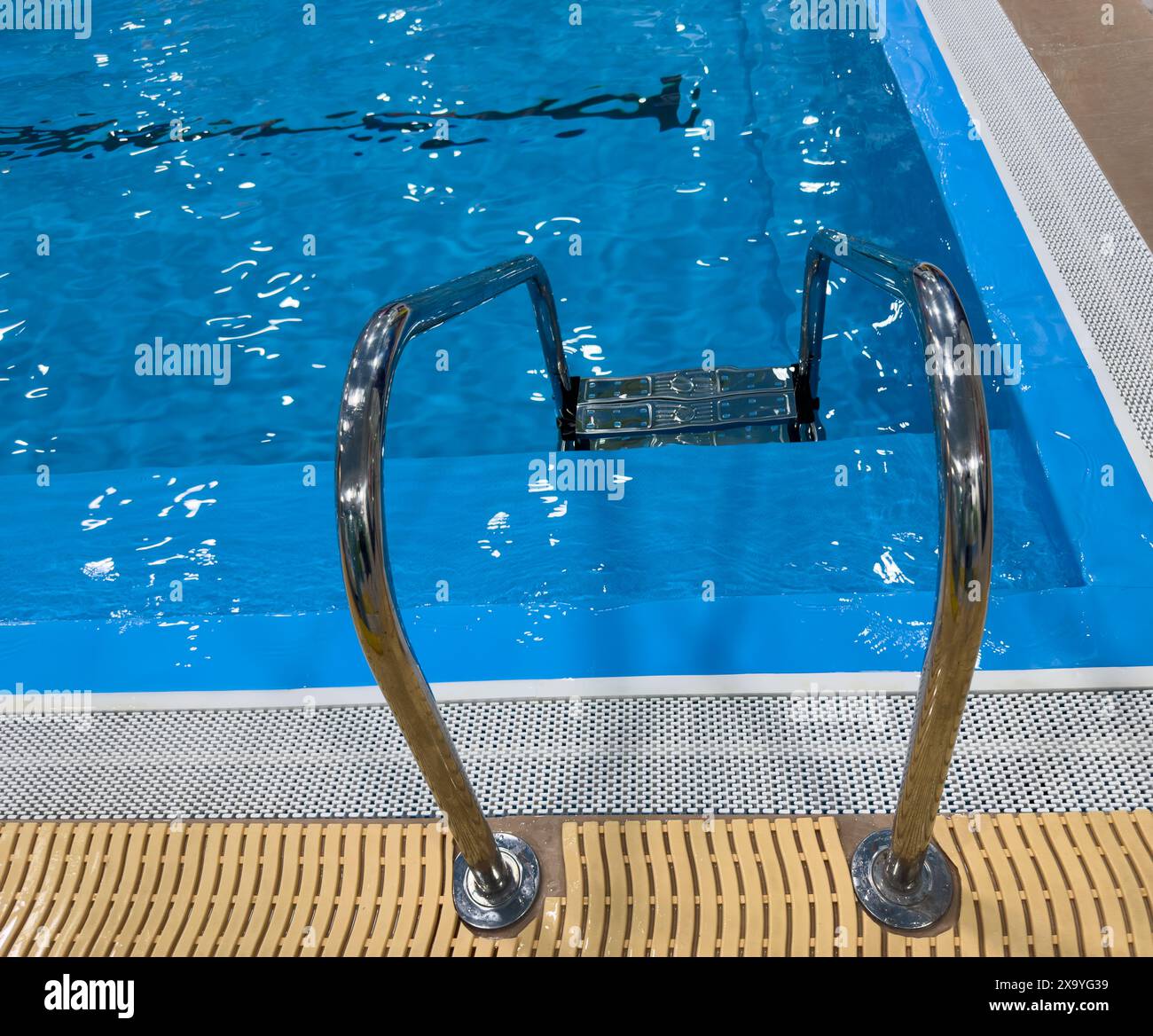 Swimmingpool mit Treppe und Wasser. Swimmingpool mit Geländer. Leiter aus Edelstahl im Pool. Haltestangen-Leiter im blauen Swimmingpool Stockfoto