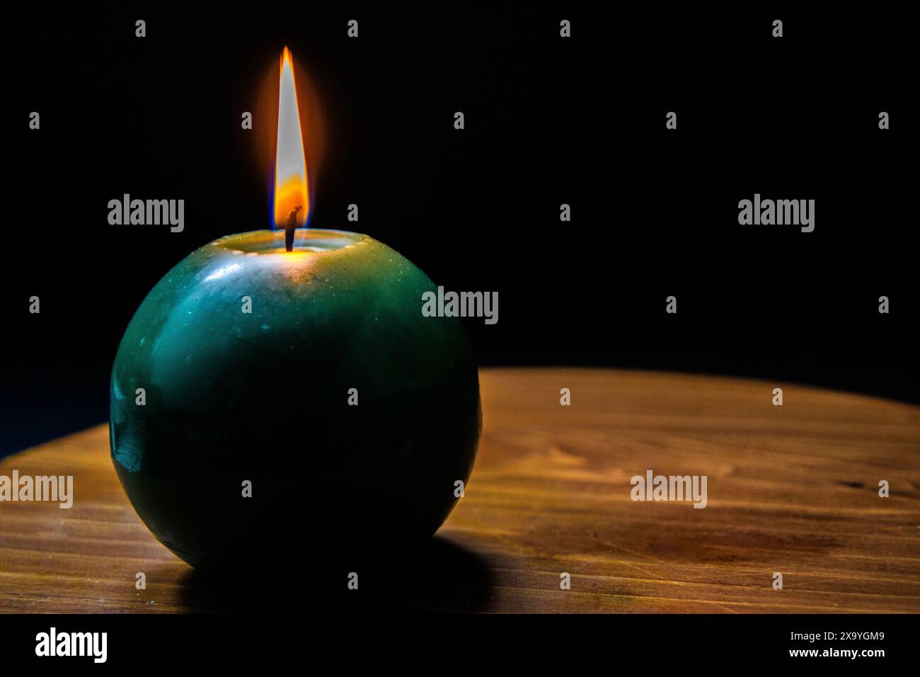 Ein grüner Apfel mit einer glühenden Kerze auf einem Tisch vor dunkler Kulisse. Stockfoto