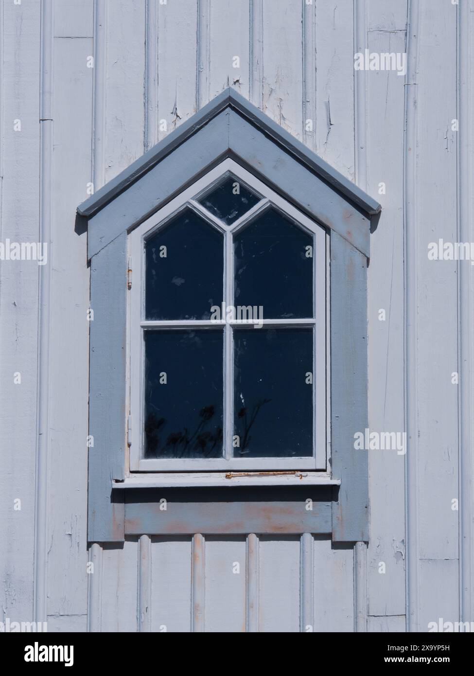 Ein verwittertes Fenster an einer Holzwand mit abblätternder Farbe Stockfoto