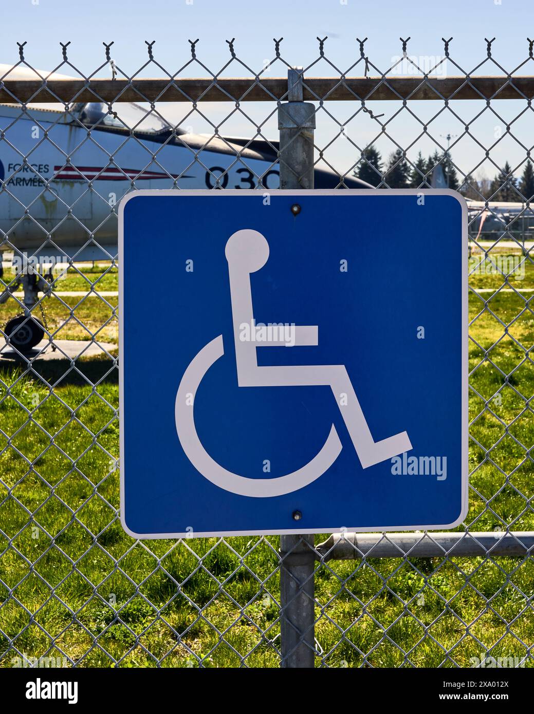 Blaues und weißes Schild mit dem Symbol für eine Person im Rollstuhl auf einem Maschendrahtzaun, das anzeigt, dass ein Park behindertengerecht ist. Stockfoto