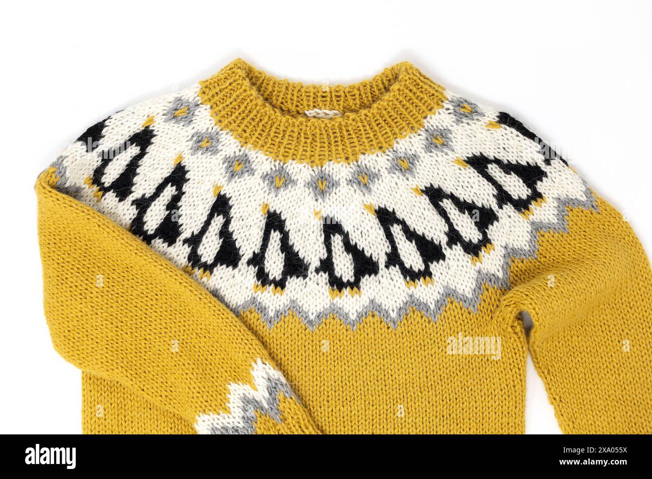 Flachbild-Fotografie eines gelben weißen, schwarzen, isländischen Strickpullovers für Kinder mit Pinguin-Muster, einer Passe und einem gerippten Nackenbund auf einem weißen Hintergrund Stockfoto