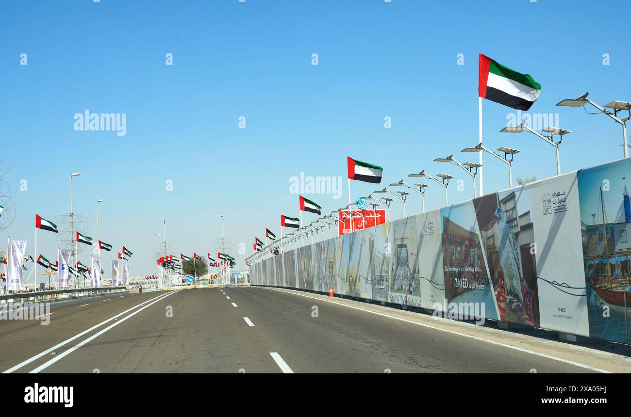 Abu Dhabi, VAE, 11. januar. 2024.- Blick auf eine Dubai Autobahn mit vielen Autos und Flaggen an der Seite. Hghway und Nationalflaggen der vereinigten staaten Stockfoto