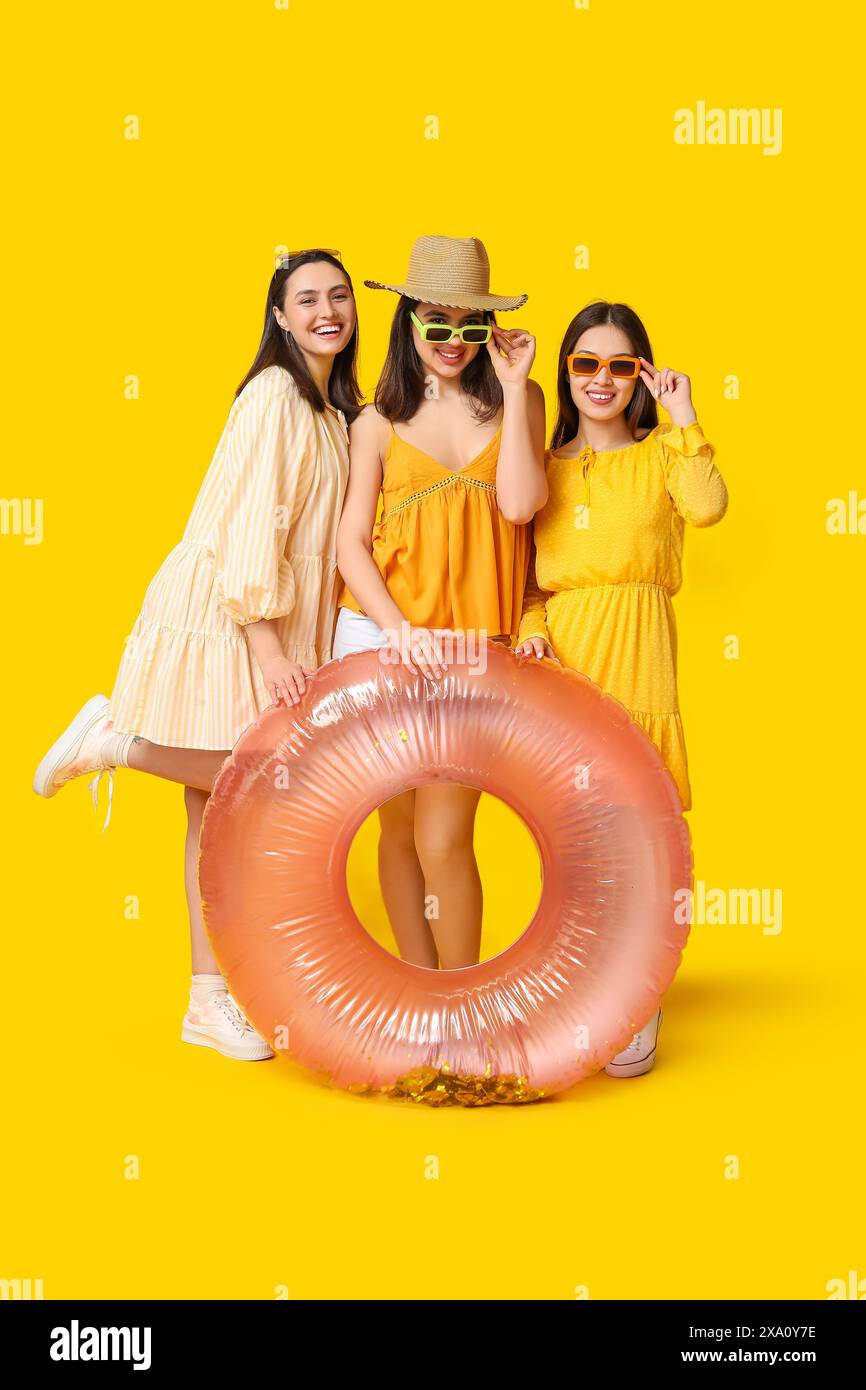 Schöne junge Frauen mit aufblasbarem Ring auf gelbem Hintergrund. Sommerparty Stockfoto