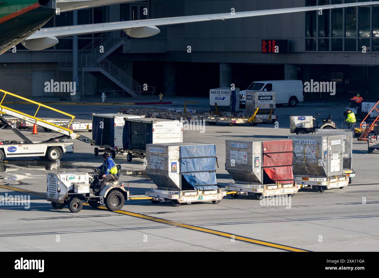 Los Angeles, Kalifornien, USA - 12. Januar 2024: Flughafenarbeiter, der einen kleinen Traktor fährt, der Frachtcontainer am internationalen Flughafen Los Angeles zieht Stockfoto