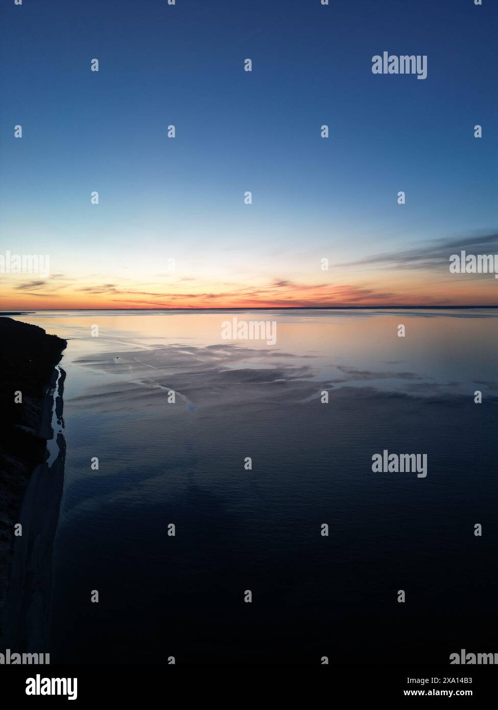 Ein ruhiger See bei Sonnenaufgang mit Orangen-, Blau- und Schwarztönen, die sich im Wasser spiegeln Stockfoto