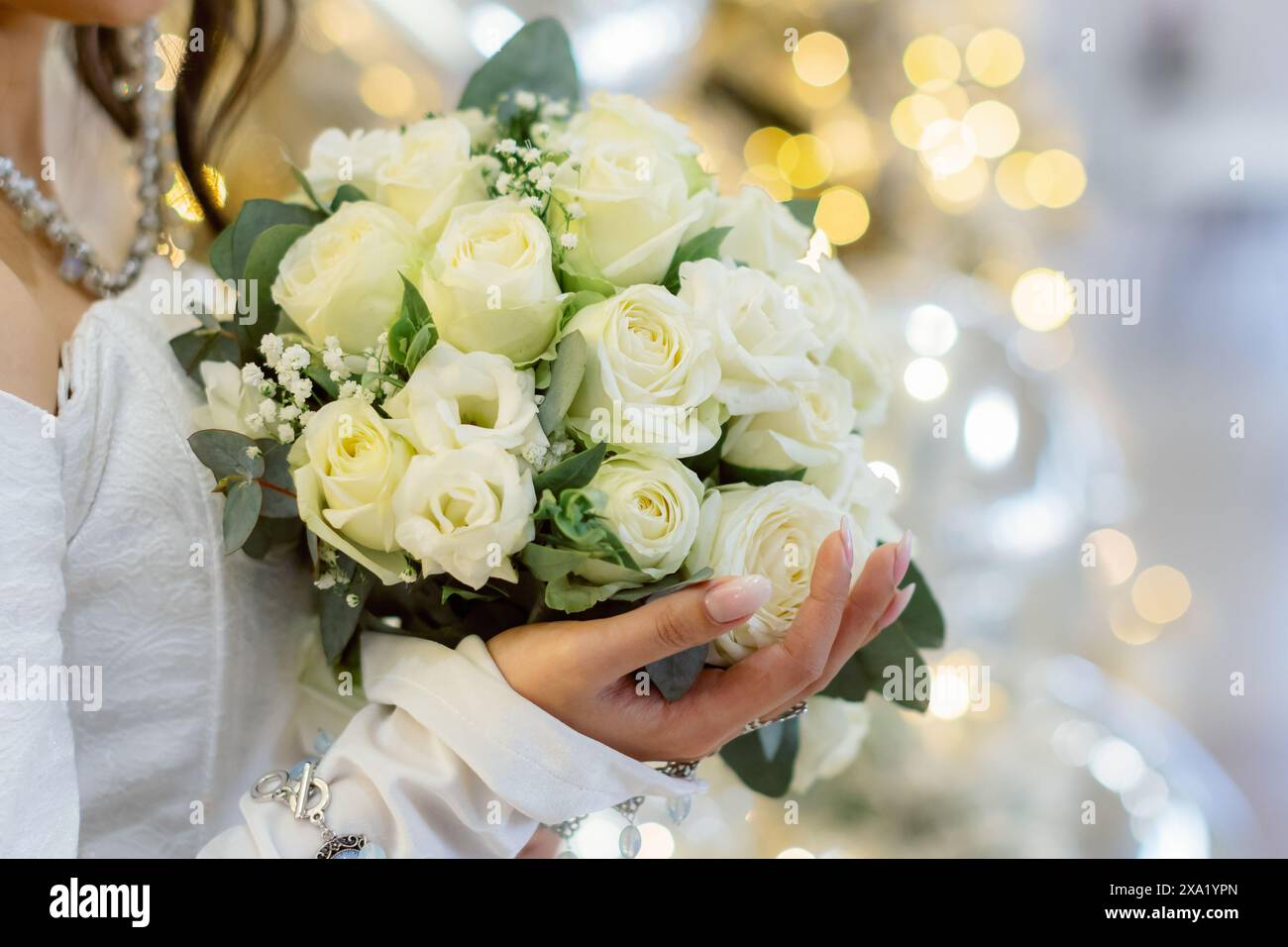 Die Frau, die einen Hochzeitsstrauß mit goldenem Bokeh-Hintergrund hält Stockfoto