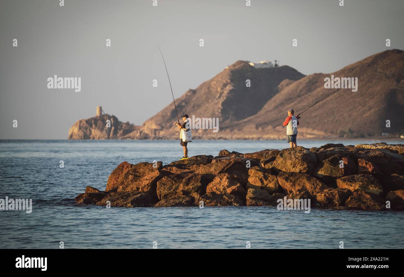 Zwei Männer fischen an einem felsigen Ufer. Das Wasser ist ruhig und der Himmel ist klar. Fischer nutzen den Sonnenaufgang zum Fischen. Daten 28-9-23. Mojacar. Stockfoto