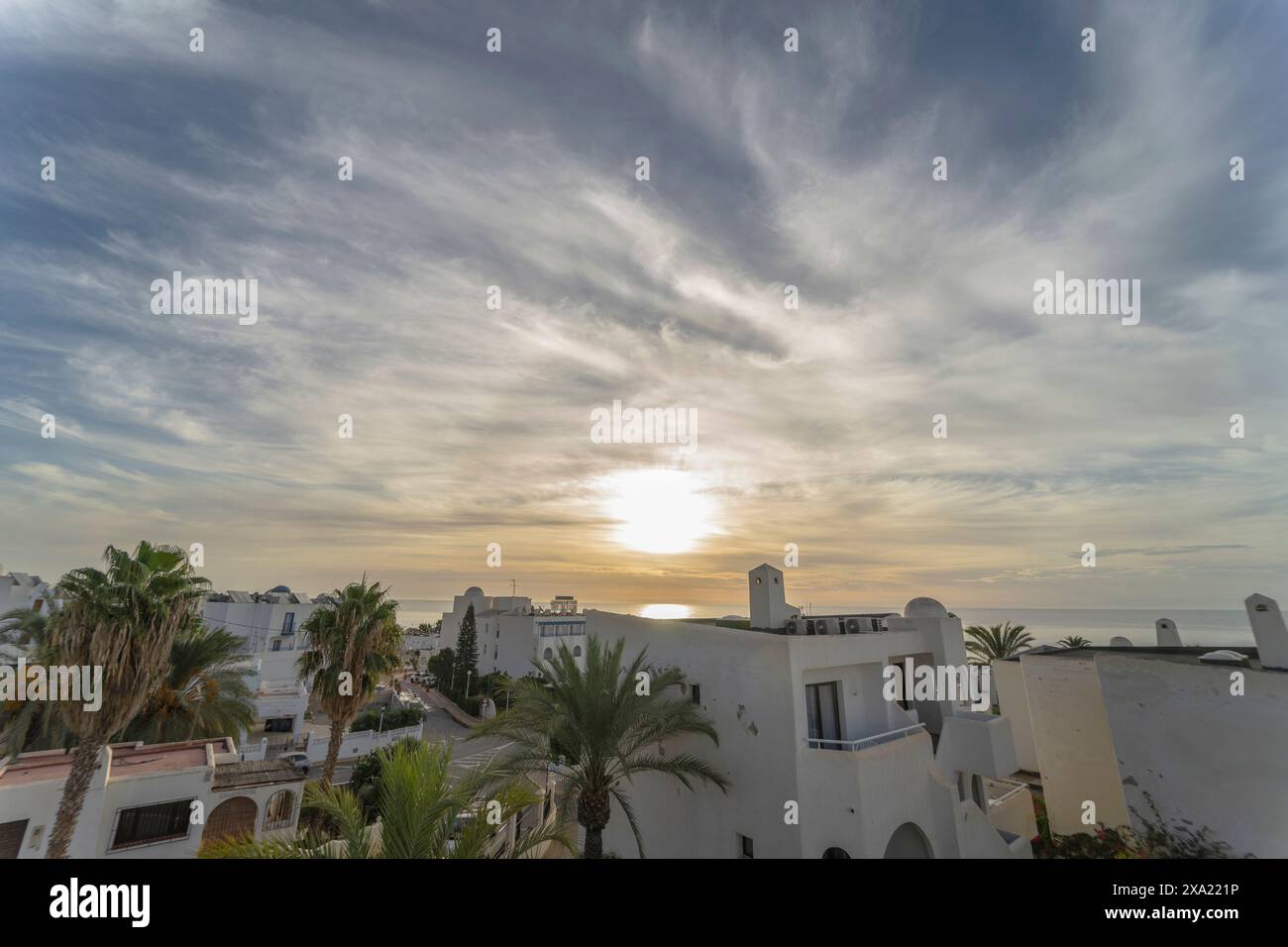 Ein beeindruckender Sonnenaufgang entfaltet sich über Mojacar, eingerahmt von Palmen und Gebäuden. Der Himmel, geschmückt mit hohen Zirruswolken, zeigt den Sonnenuntergang Stockfoto