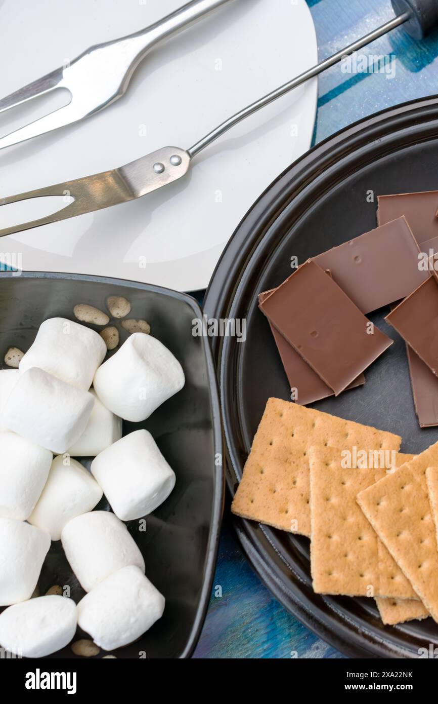 Zutaten für Smores... Blick von oben nach unten mit Schokolade, graham Cracker, Marshmallows und Gabeln zum Rösten von Marshmallows. Stockfoto