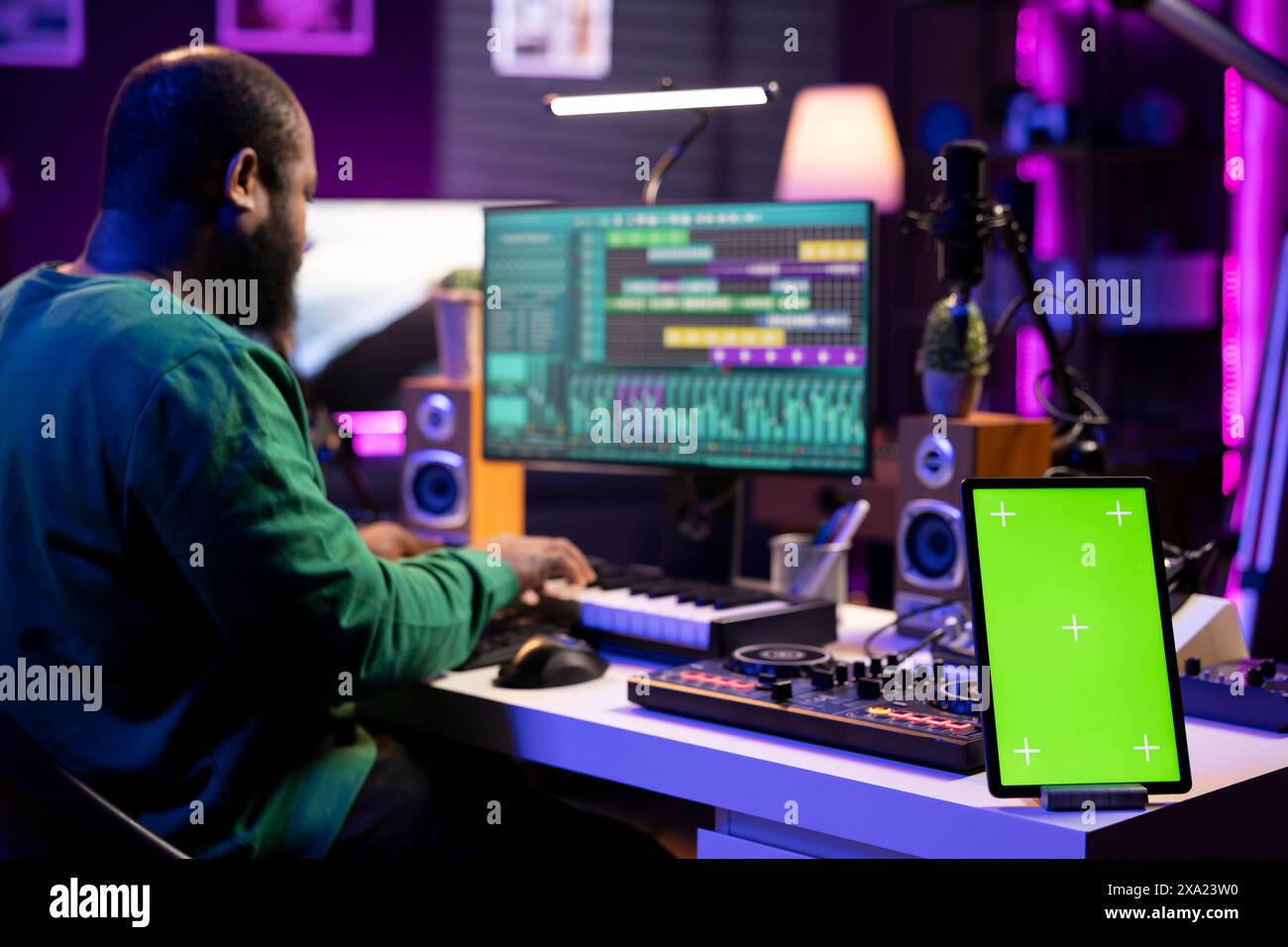 Der Komponist bearbeitet seine Audiodateien und Aufnahmen mit der daw-Software und sitzt neben einem Greenscreen-Display. Ein erfahrener Tontechniker verwendet Misch- und Mastering-Geräte, um neues Material herzustellen. Stockfoto